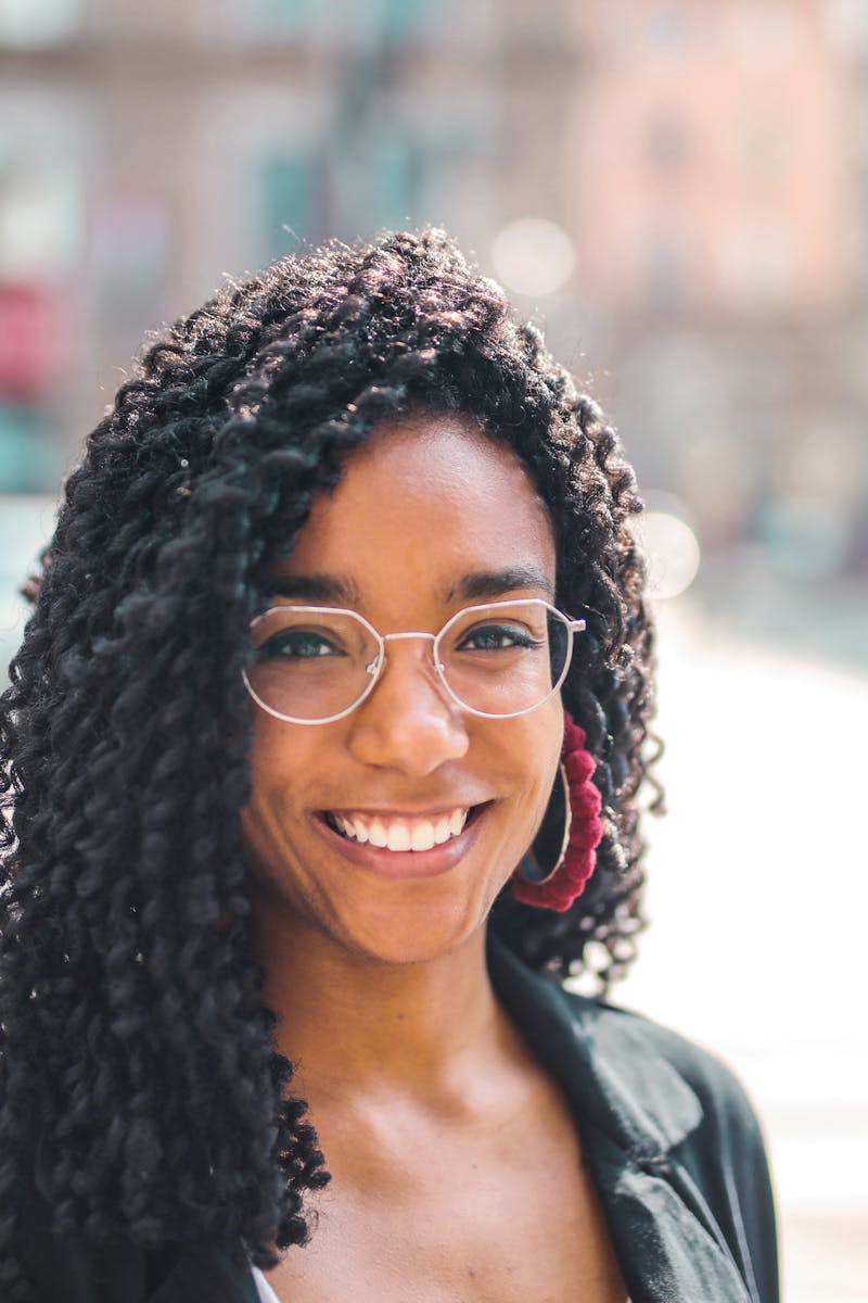 Attractive young woman with curly hair and eyeglasses smiling on a sunny day in the city.